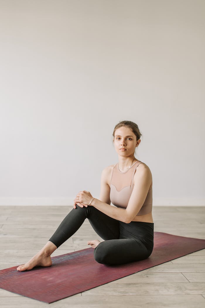 A young woman practicing yoga indoors, seated on a mat, promoting a healthy lifestyle.