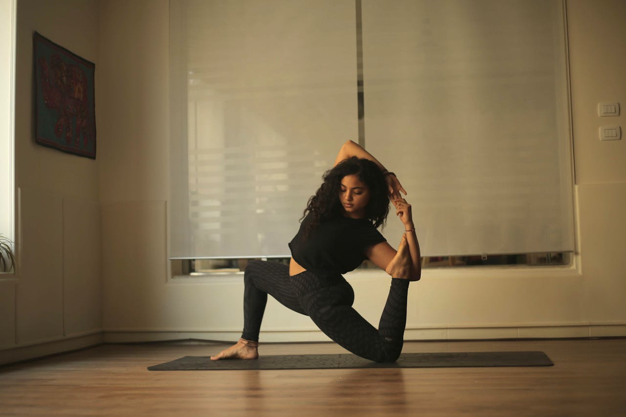 A woman in black attire performing a yoga pose on a mat indoors, showcasing flexibility and balance.